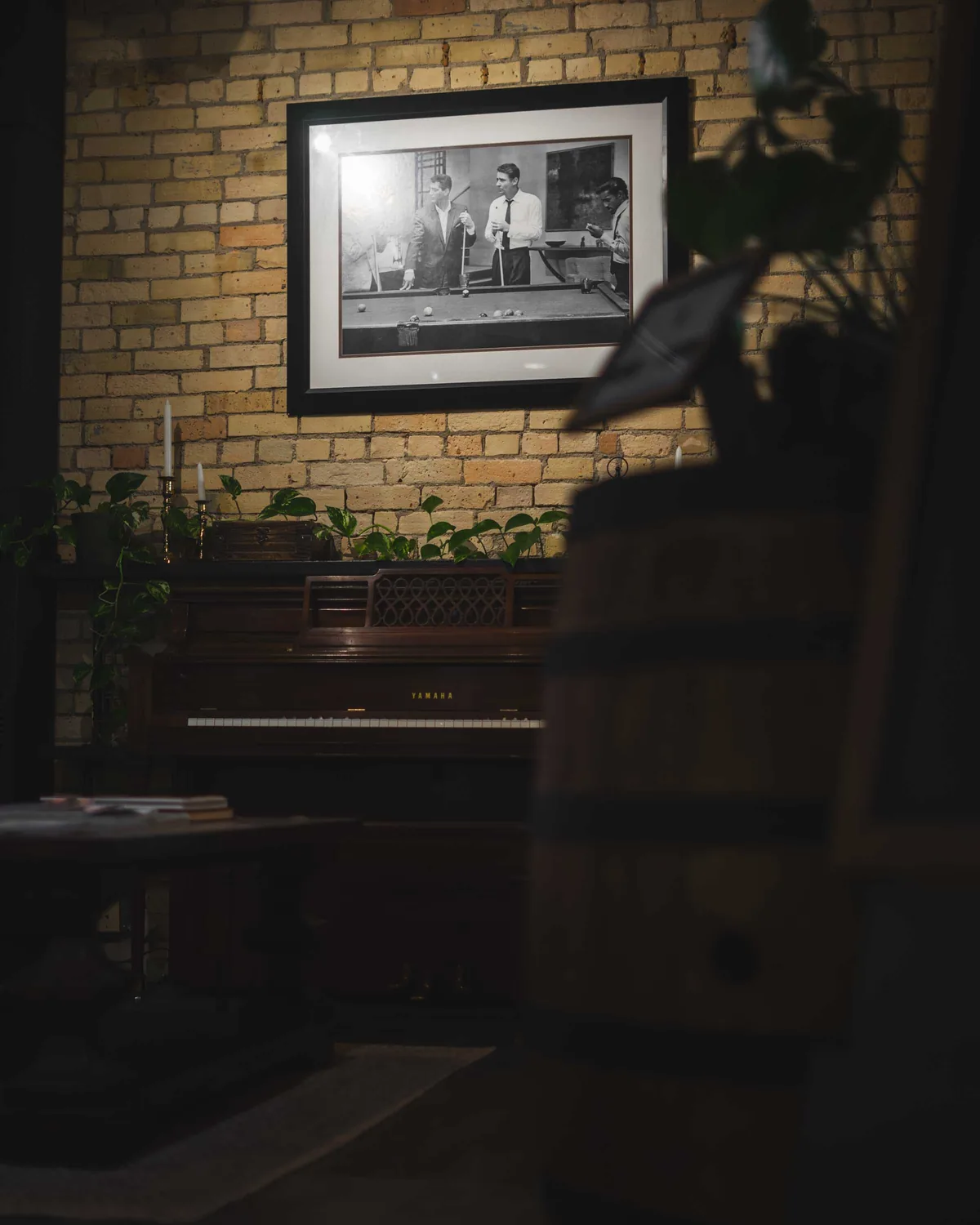 Upright piano, candles and a framed photograph on the exposed brick wall of the lounge at Studio AZ Barbershop